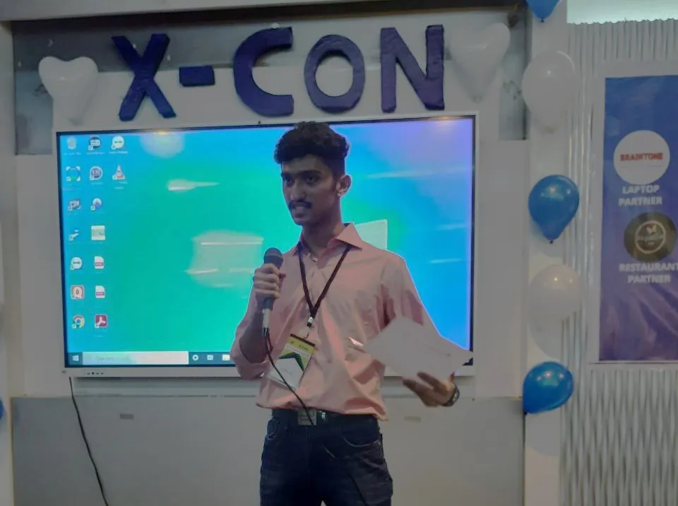 Sharath Pai speaking into a microphone on stage at X-CON